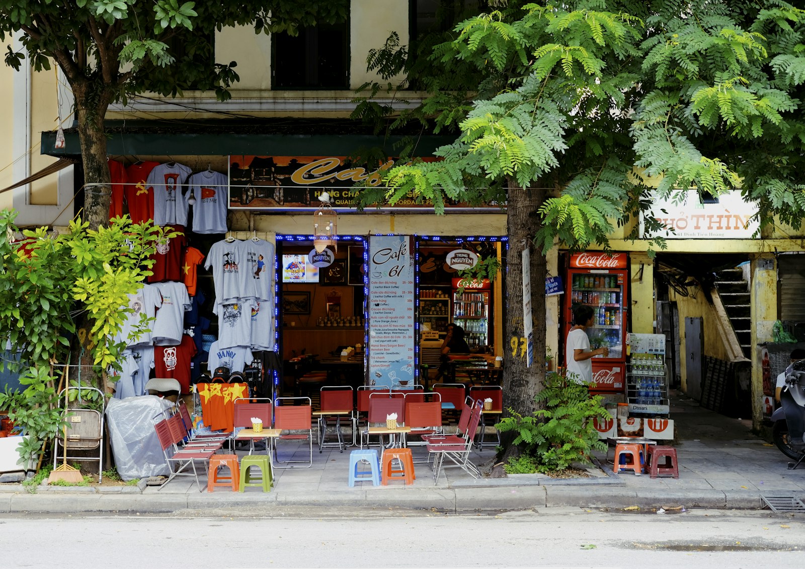 Vỉa hè quán cafe Việt — ghế nhựa đỏ, biển hiệu, cây xanh